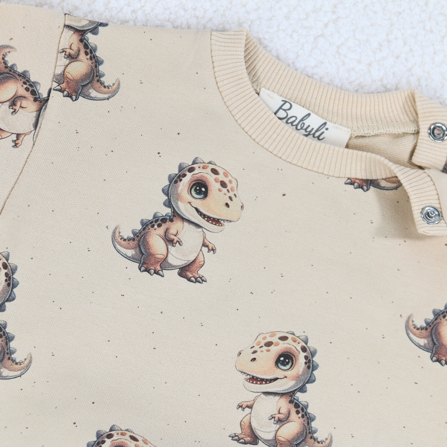 Close-up of cream baby sweatshirt with dinosaur print