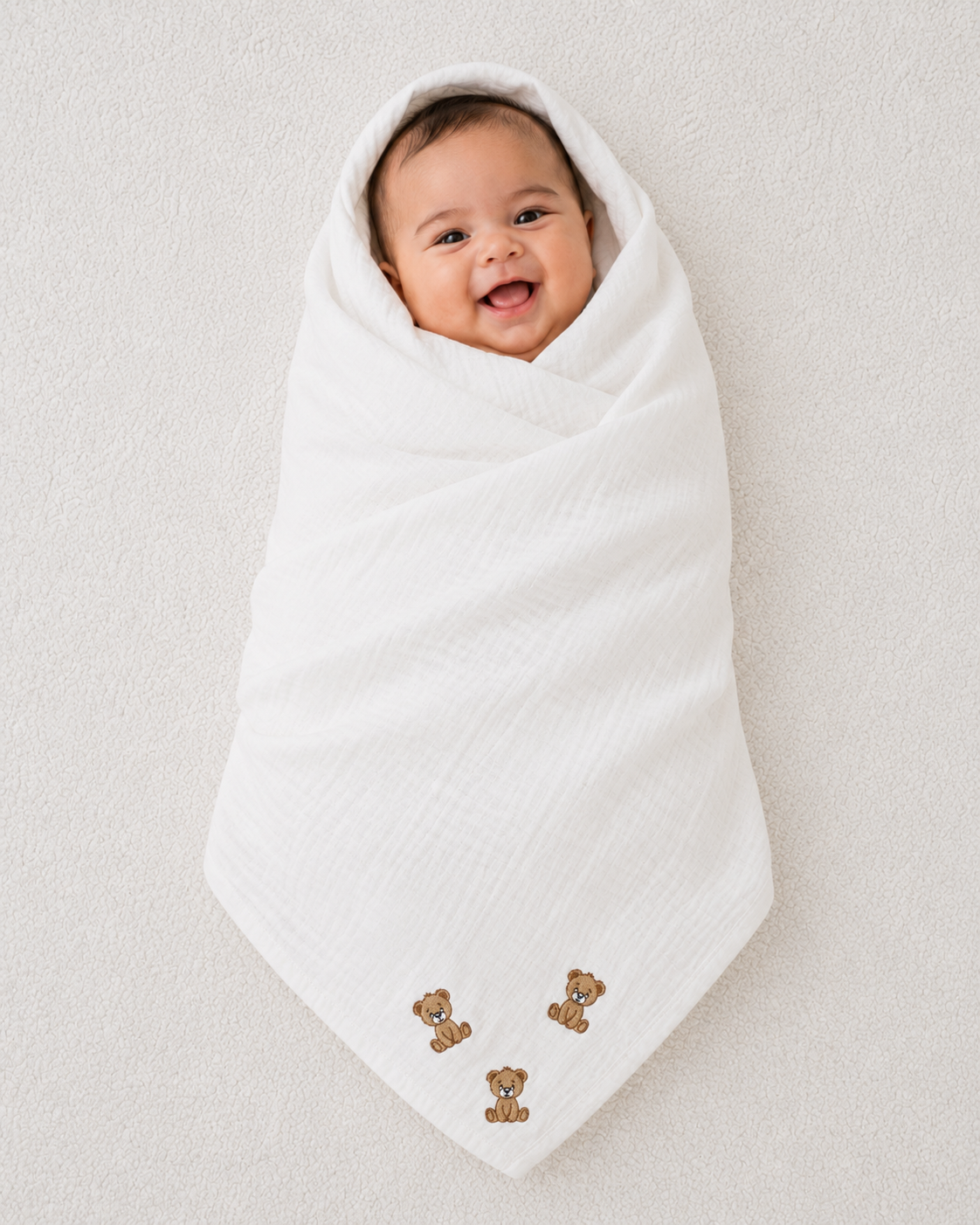 Smiling baby swaddled in soft white muslin blanket with embroidered teddy bear design