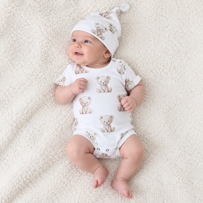 Baby lying down wearing a white cotton bodysuit with teddy bear print and matching hat, Babyli baby bodysuit set