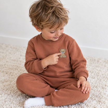 Toddler boy wearing Babyli brown fleece tracksuit, touching the embroidered teddy bear