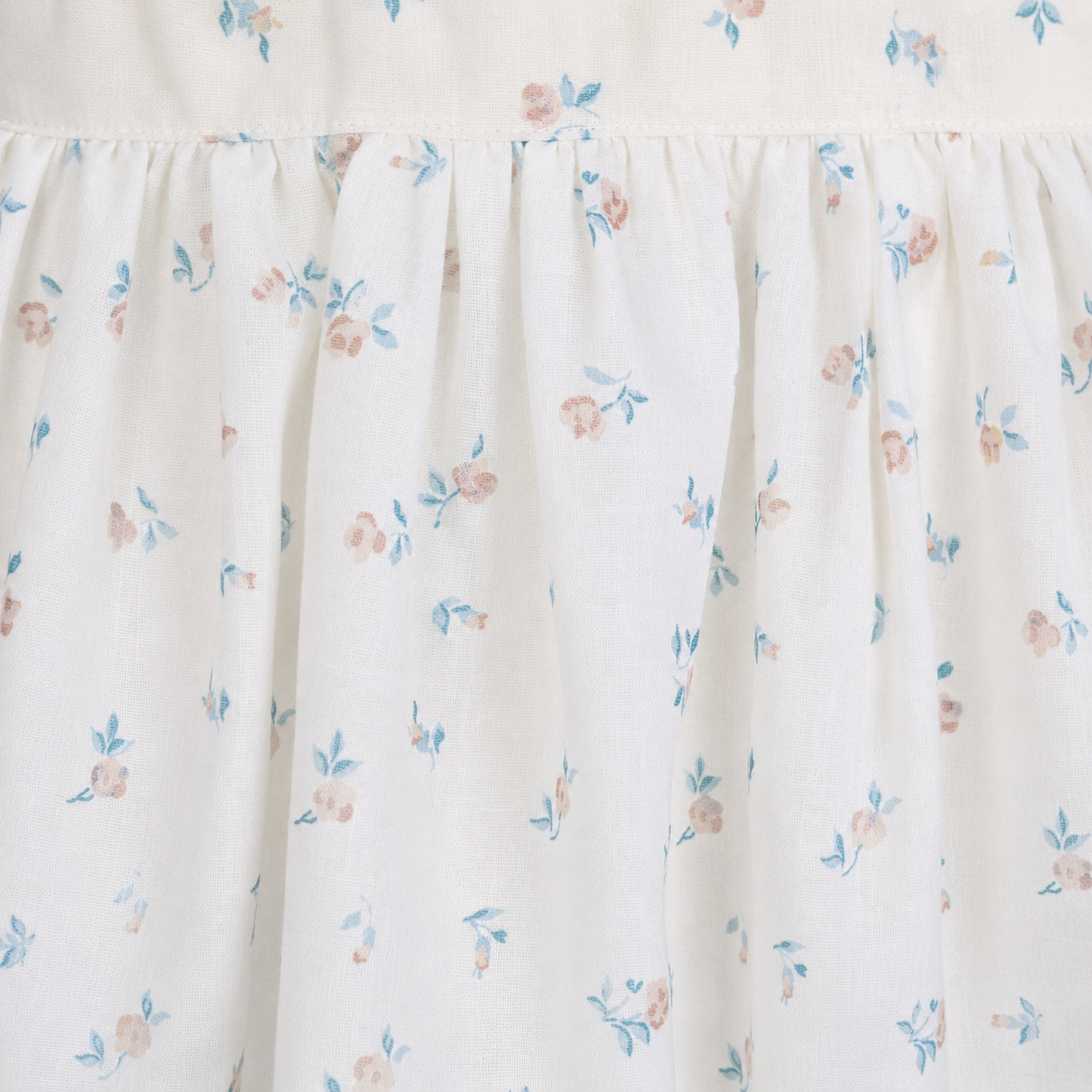Girls cream floral print dress close up showing smocked bodice detail and puff sleeves with wicker basket and rose styling by Babyli, boutique girls dresses UK