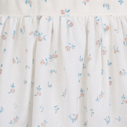 Girls cream floral print dress close up showing smocked bodice detail and puff sleeves with wicker basket and rose styling by Babyli, boutique girls dresses UK