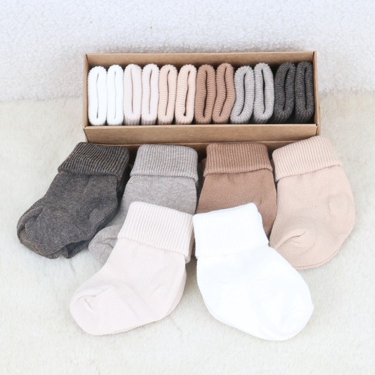 Folded pairs of newborn baby socks in taupe, grey and neutral tones beside their gift box