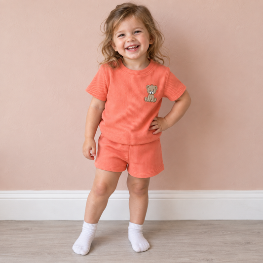 Toddler wearing Babyli orange teddy bear embroidered t-shirt and shorts set, candid photo