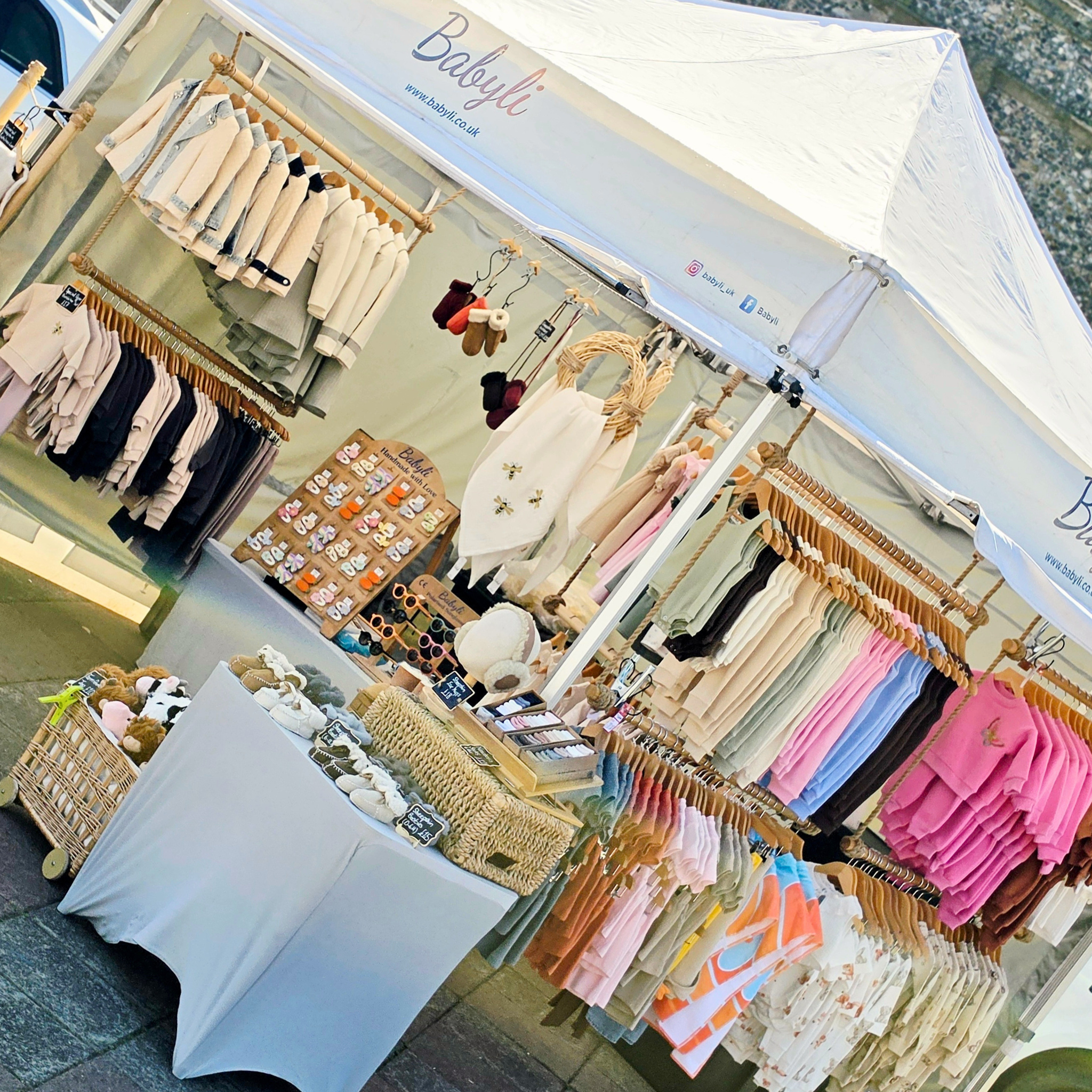 Babyli boutique market stall at St Albans displaying baby and toddler clothing, shoes and accessories including pink tops, sandals and sheepskin products