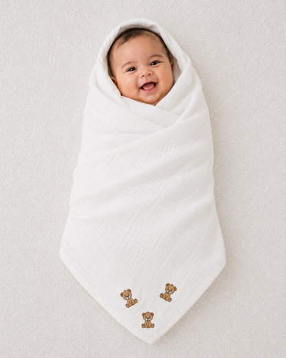 Smiling baby swaddled in soft white muslin blanket with embroidered teddy bear design by Babyli, boutique baby muslin blanket UK