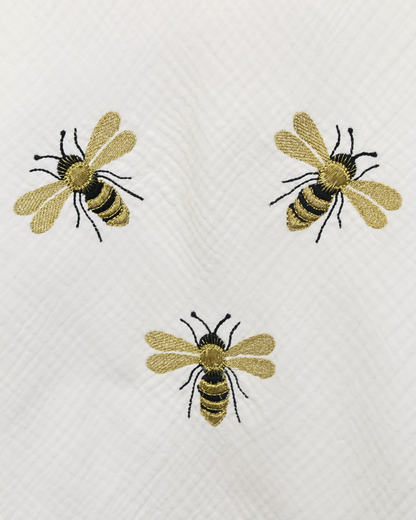 White muslin baby blanket with embroidered bee details.