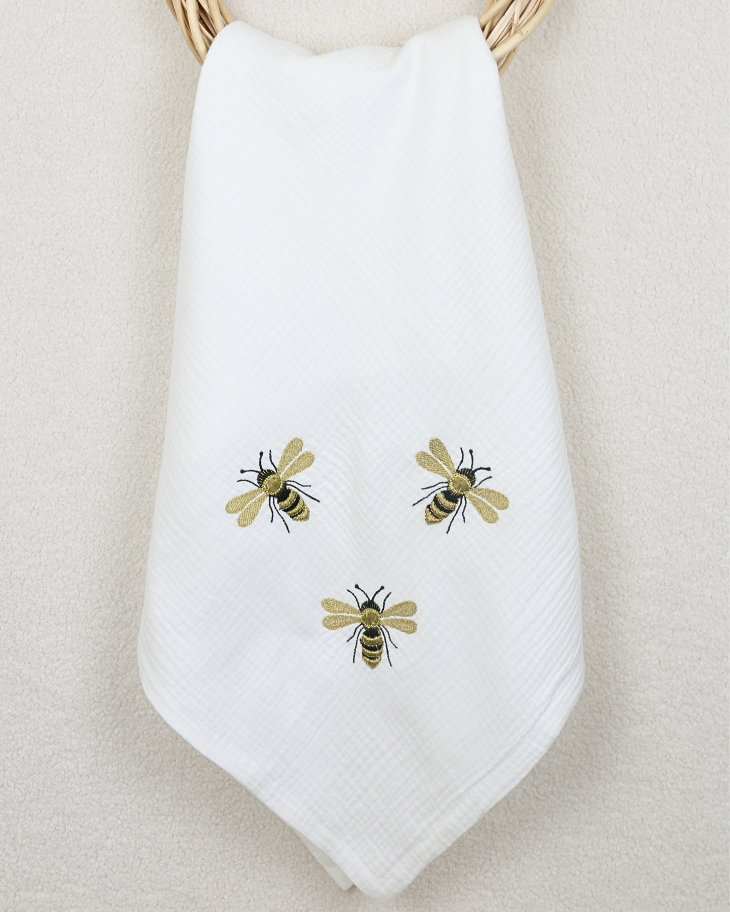 White muslin baby blanket with embroidered bee details.