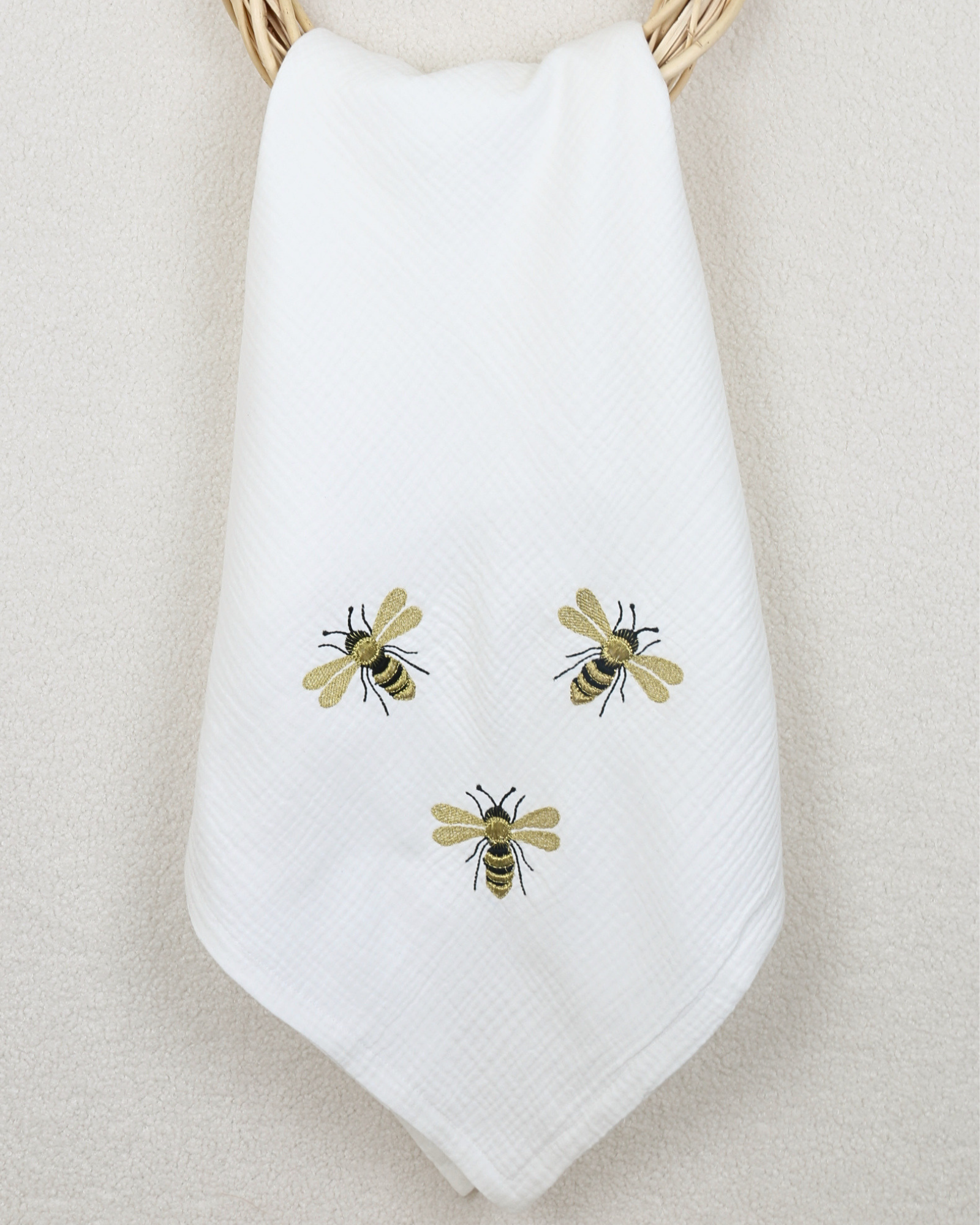 White muslin baby blanket with embroidered bee details.