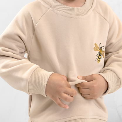 Child wearing beige sweatshirt with bumblebee embroidery