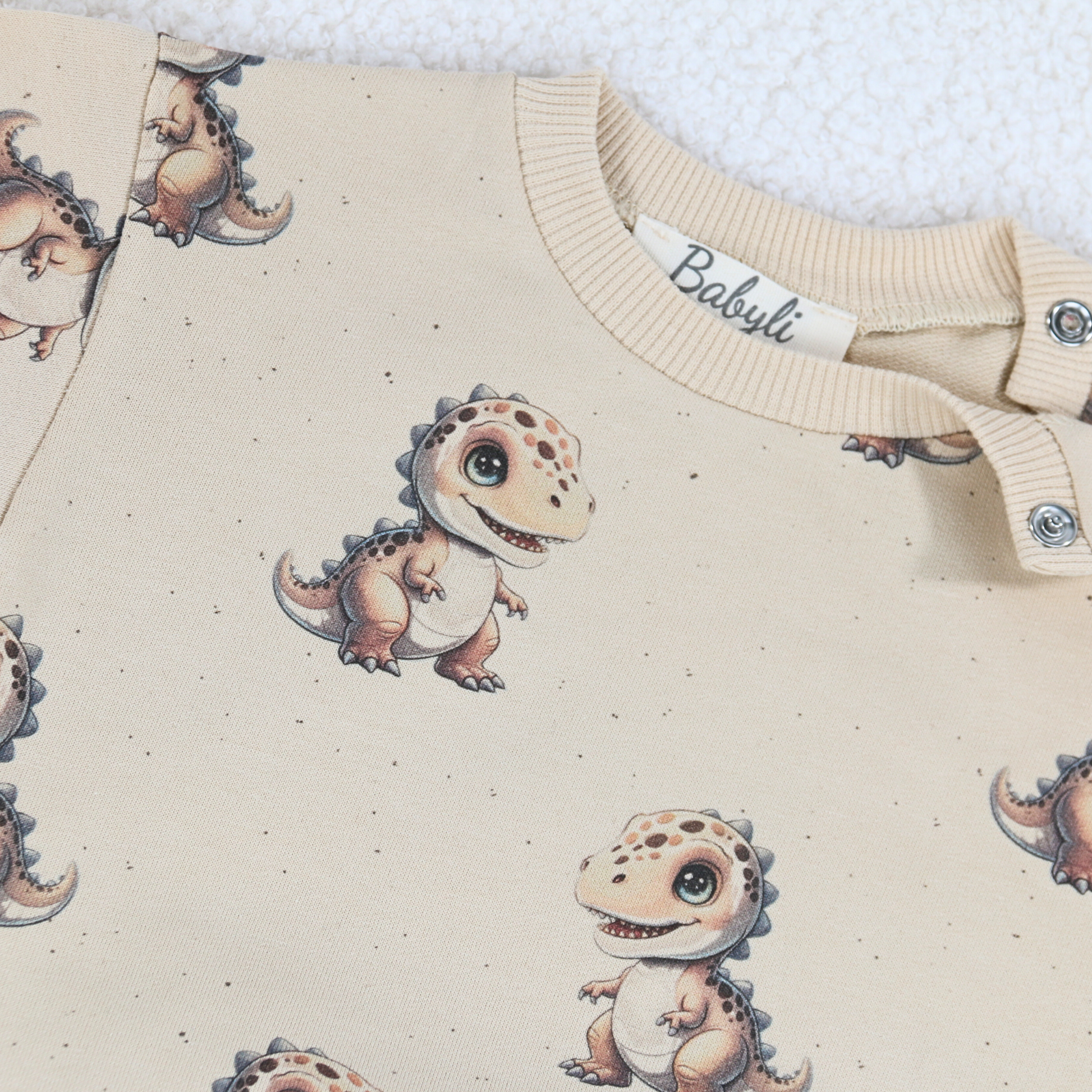 Close-up of cream baby sweatshirt with dinosaur print