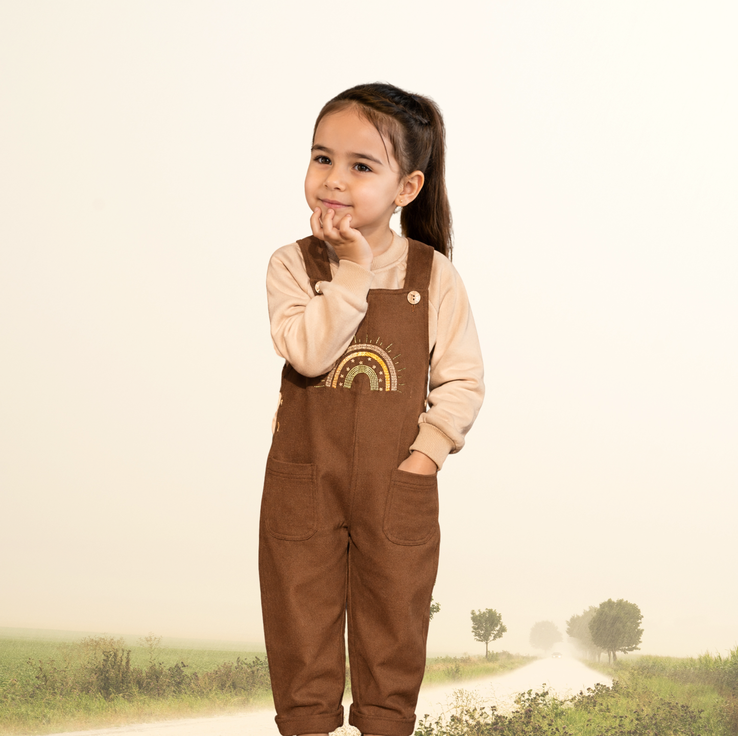 Brown baby dungarees with rainbow embroidery detail.