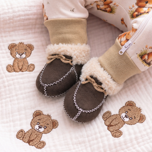 Baby wearing brown sheepskin booties in a woodland-themed sleepsuit