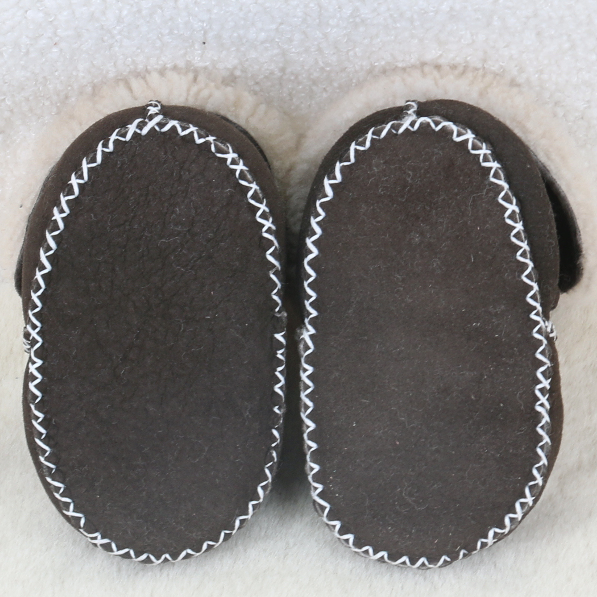 Soles of brown sheepskin baby booties showing handmade-inspired stitching
