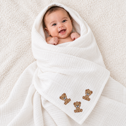 Baby wrapped in a white muslin blanket with three embroidered teddy bear details.