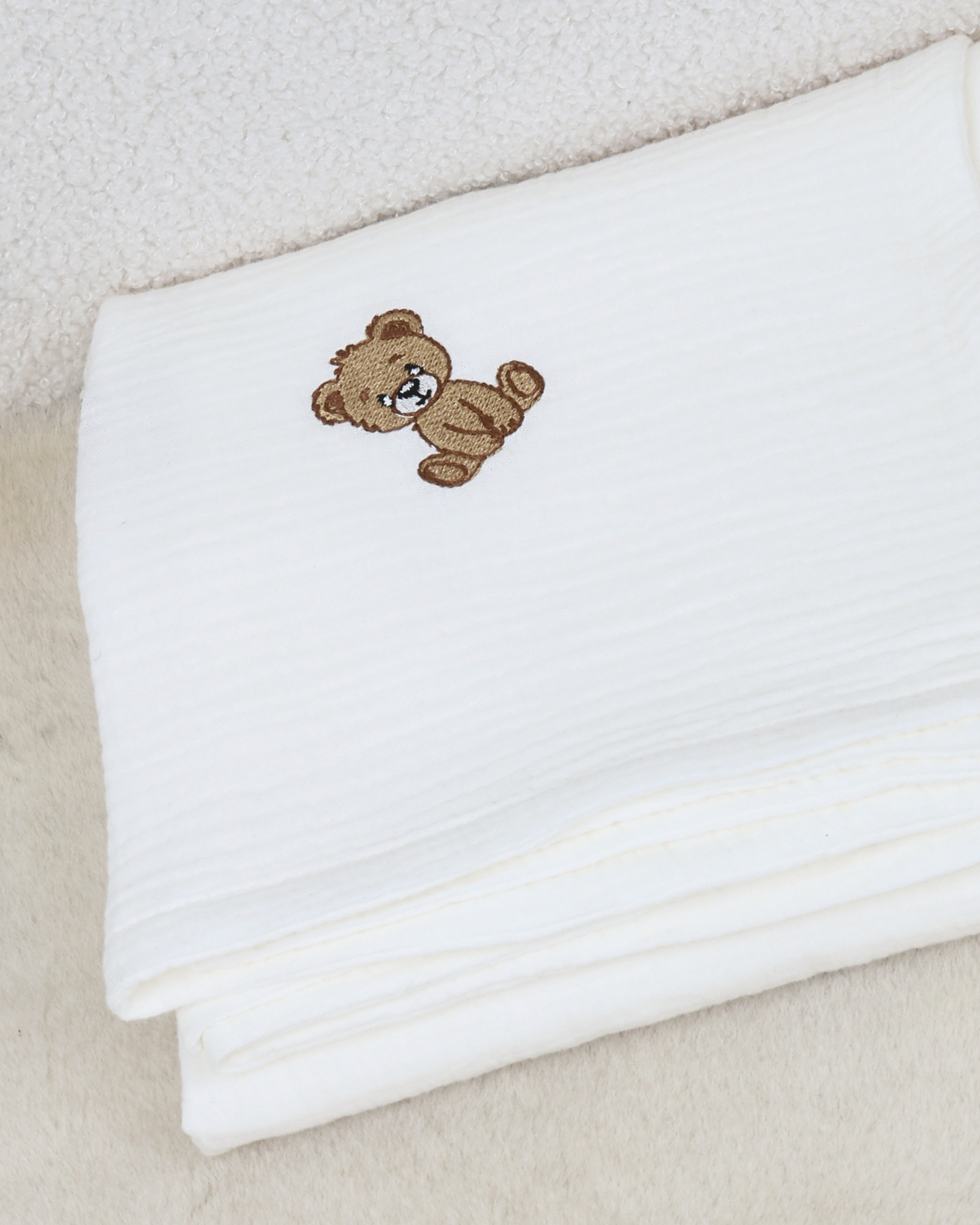 White muslin baby blanket with embroidered teddy bear details.