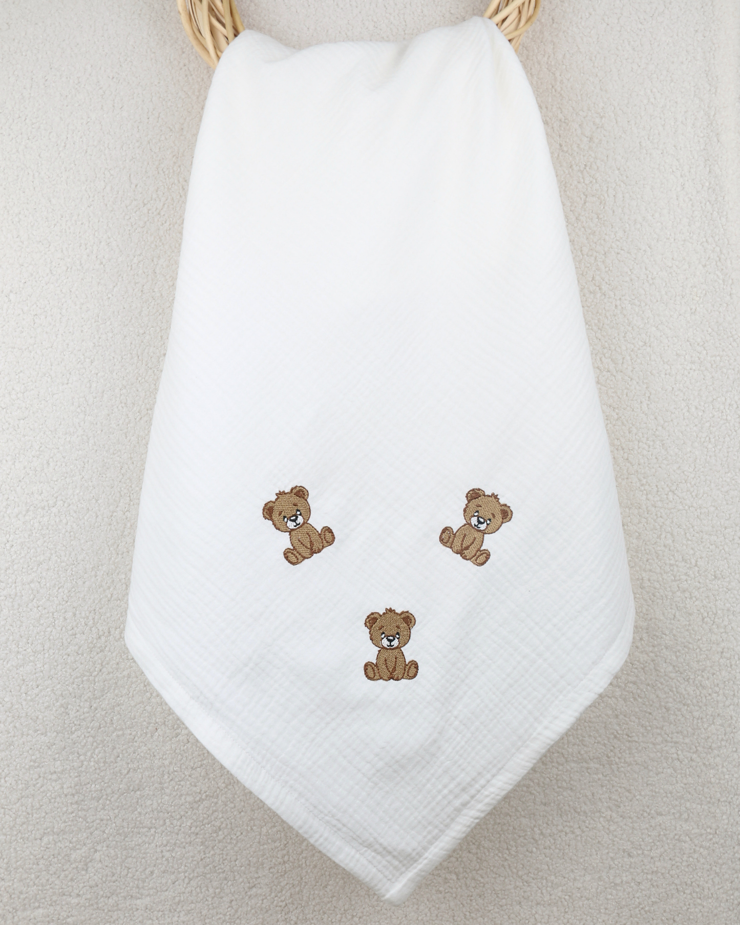 White muslin baby blanket with embroidered teddy bear details.