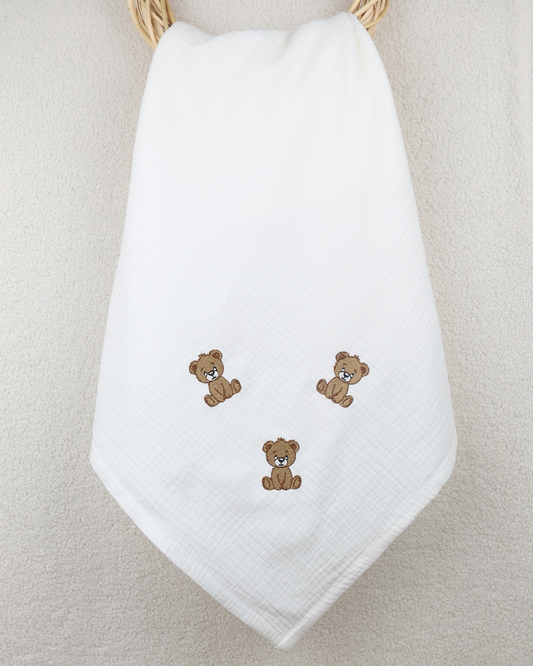 White muslin baby blanket with embroidered teddy bear details.