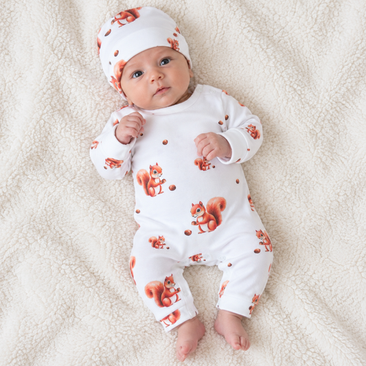 Baby lying down wearing a white cotton romper with squirrel print and matching hat, Babyli newborn romper set