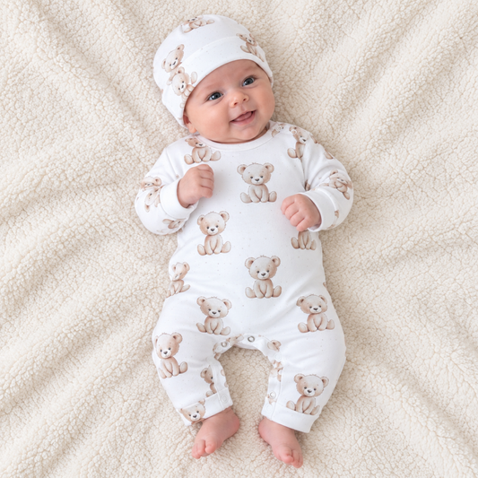 Baby lying down wearing a white cotton romper with teddy bear print and matching hat, Babyli newborn romper set